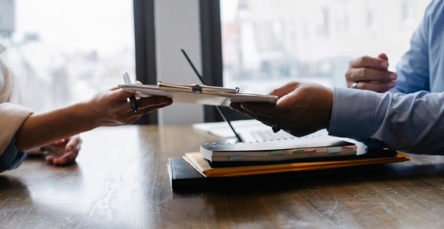 Crop anonymous ethnic woman passing clipboard to office worker