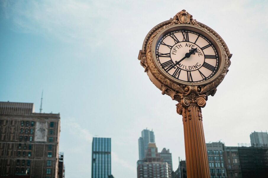 From below of aged metal clock tower located in city center with high towers