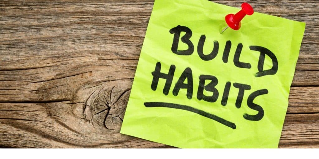 Sticky note with 'Build Habits' pinned to a wooden board, emphasizing the importance of developing consistent habits for motivation